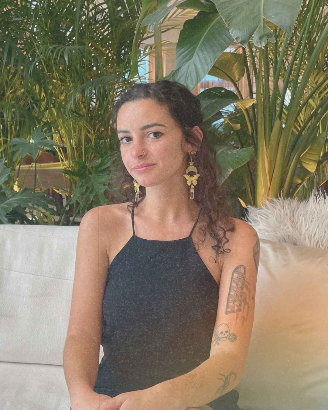 Isabella DeChard, cannabis wellness coach, sitting on a white couch in front of lush green plants.