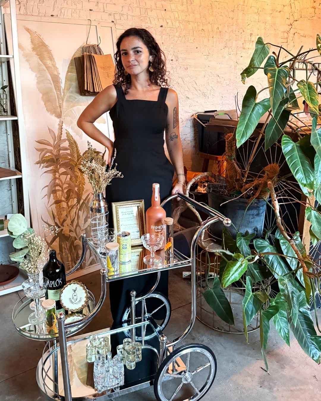 Isabella DeChard presents her mobile cannabis beverage bar cart, serving handcrafted herbal drinks in a lush, plant-filled setting.