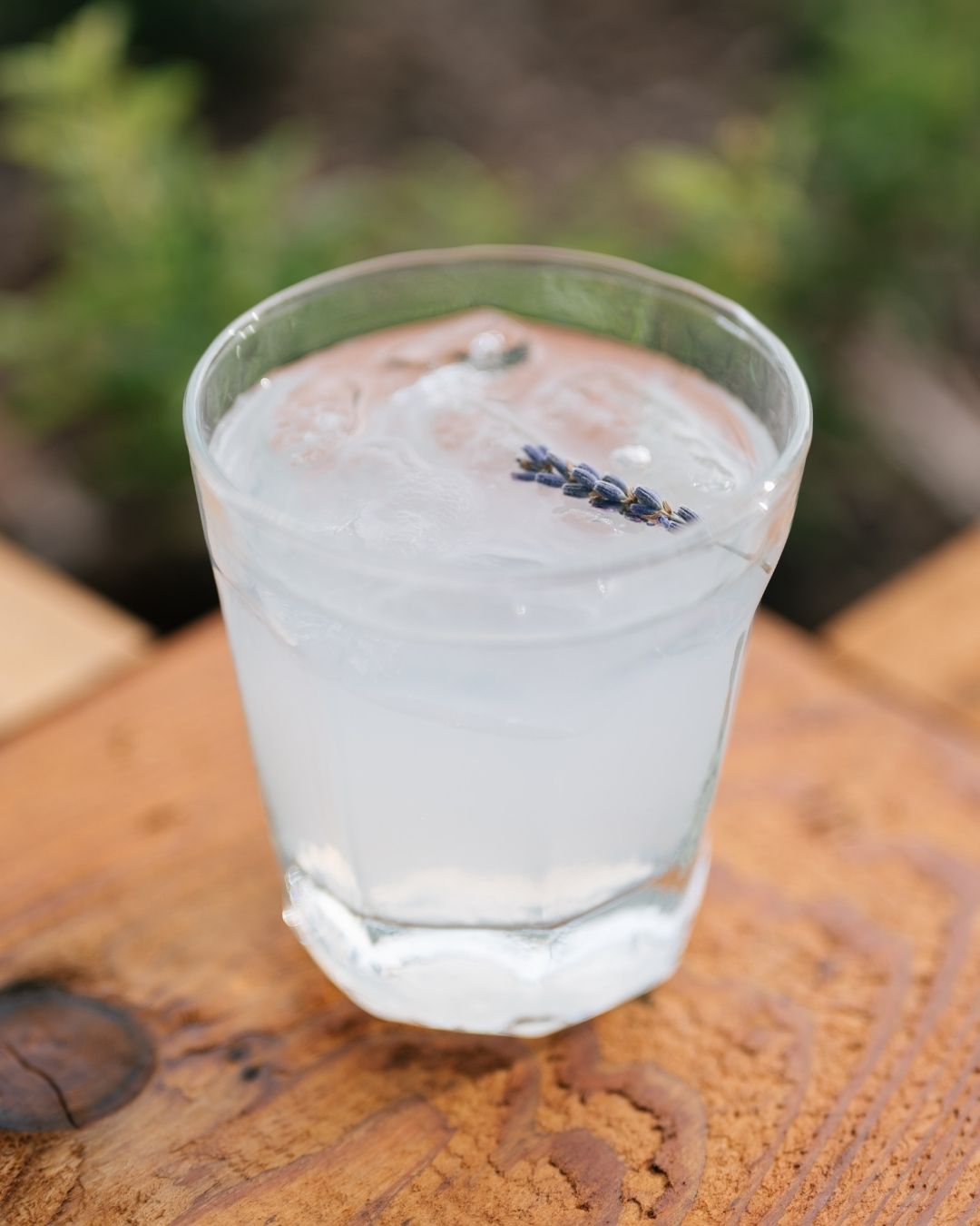 Chilled herbal drink with ice and lavender garnish in a clear glass on a wooden table, styled in natural light for a mindful wellness event.